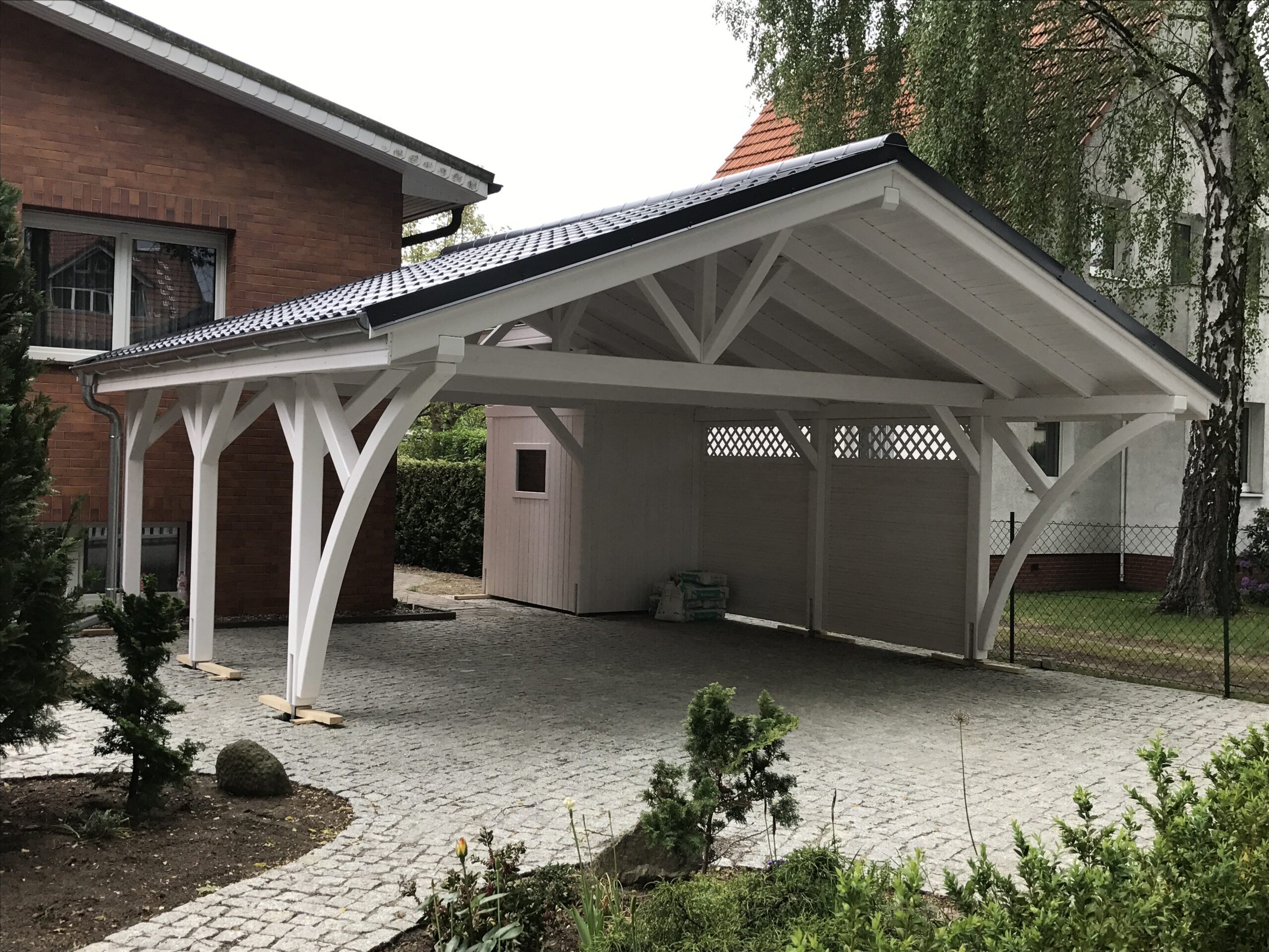 Satteldach Doppelcarport AlpineXL in Weiß mit eleganten Bögen und massiven Pfosten. Die Bretterschalung und das Vivaldi-Dach in Ziegeloptik unterstreichen handwerkliche Präzision.