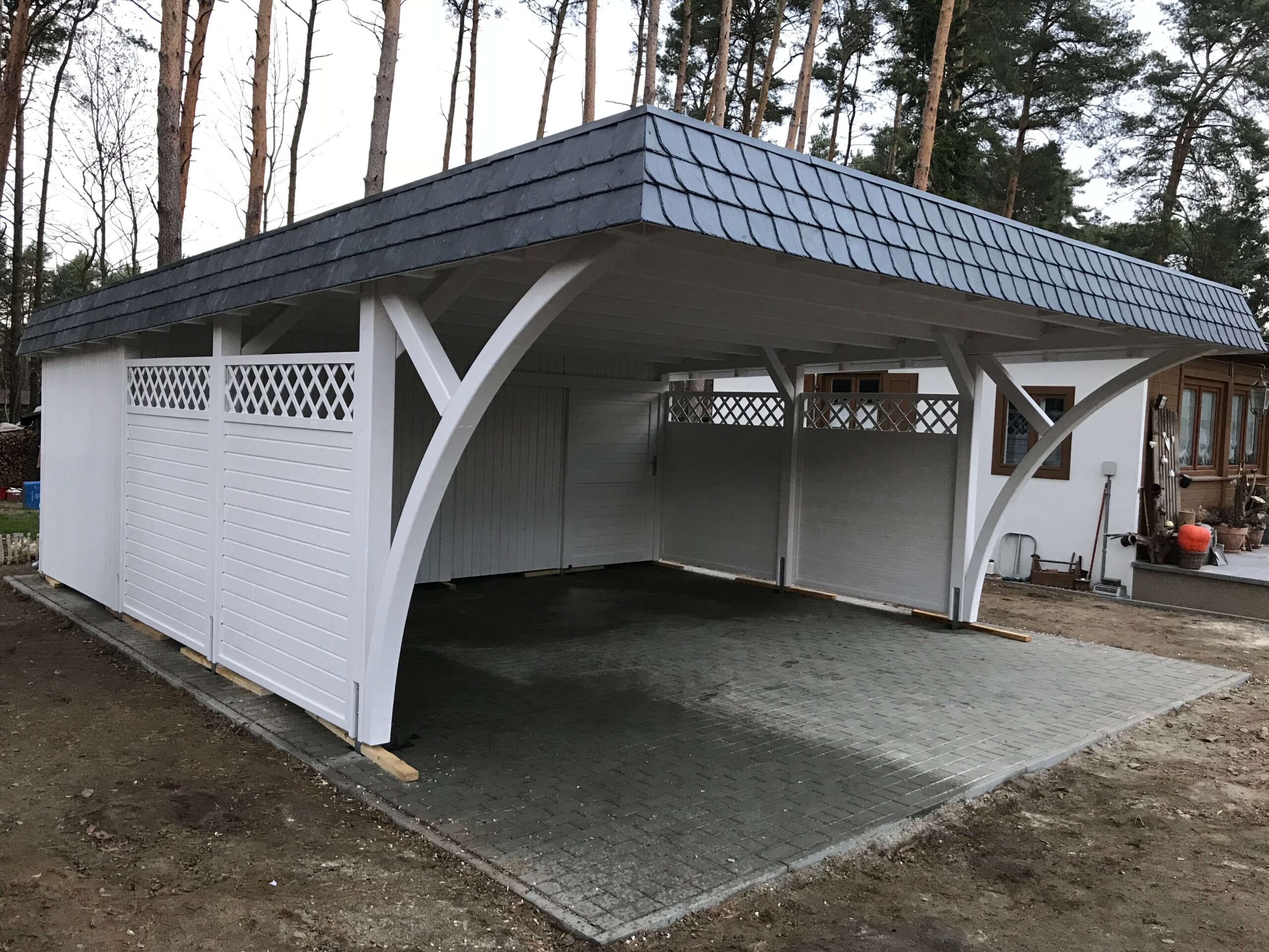Seitliche Ansicht des Elegance Duo Carports mit Bögen und Holzpaneelzaun. Die Verbindung aus dekorativen Elementen und klarer Struktur wirkt elegant und ausgewogen.