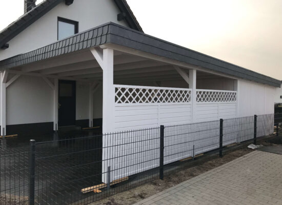 Doppelcarport mit Walmdachblende und seitlichem Zaunelement. Weiß-Anthrazit-Kombination und klare Linien betonen modernes Design und Handwerksqualität.