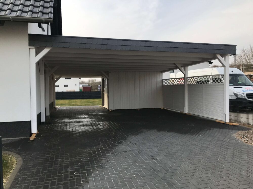 Doppelcarport mit Flachdach, weißer Struktur und anthrazitfarbenem Dachrand. Klare Proportionen und feine Holzverarbeitung prägen das Erscheinungsbild.
