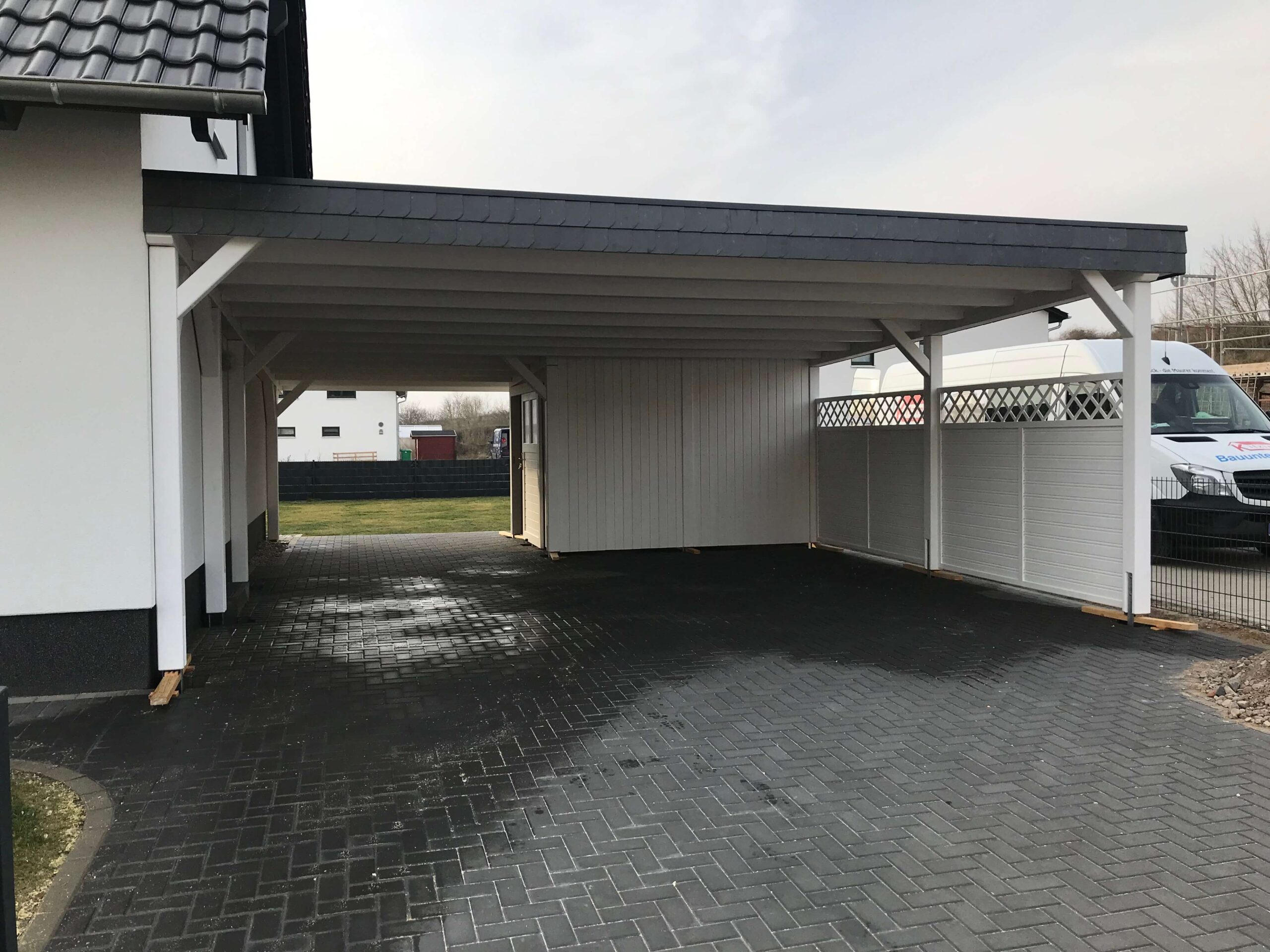 Doppelcarport mit Flachdach, weißer Struktur und anthrazitfarbenem Dachrand. Klare Proportionen und feine Holzverarbeitung prägen das Erscheinungsbild.