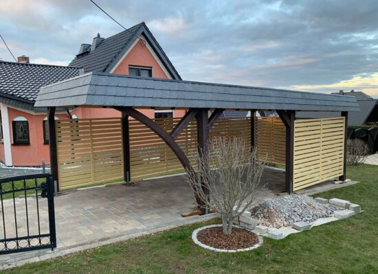 StyleLine Carport mit seitlichem Bogen, beiger Wandverkleidung und Walmdachblende in Schieferoptik. Die Kombination aus Braun und Schiefergrau wirkt warm und elegant zugleich.