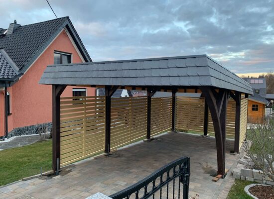 Frontansicht des StyleLine Carports mit dreireihiger Walmdachblende in Schieferoptik. Die strukturierte Oberfläche verleiht Tiefe und architektonische Eleganz.