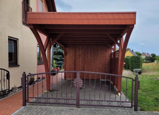 Flachdach Einzelcarport mit zwei Rundbögen, Walmdachblende in Ziegeloptik und Holz in Mahagonifarben imprägniert. Die harmonische Front betont Stabilität und handwerkliche Präzision.