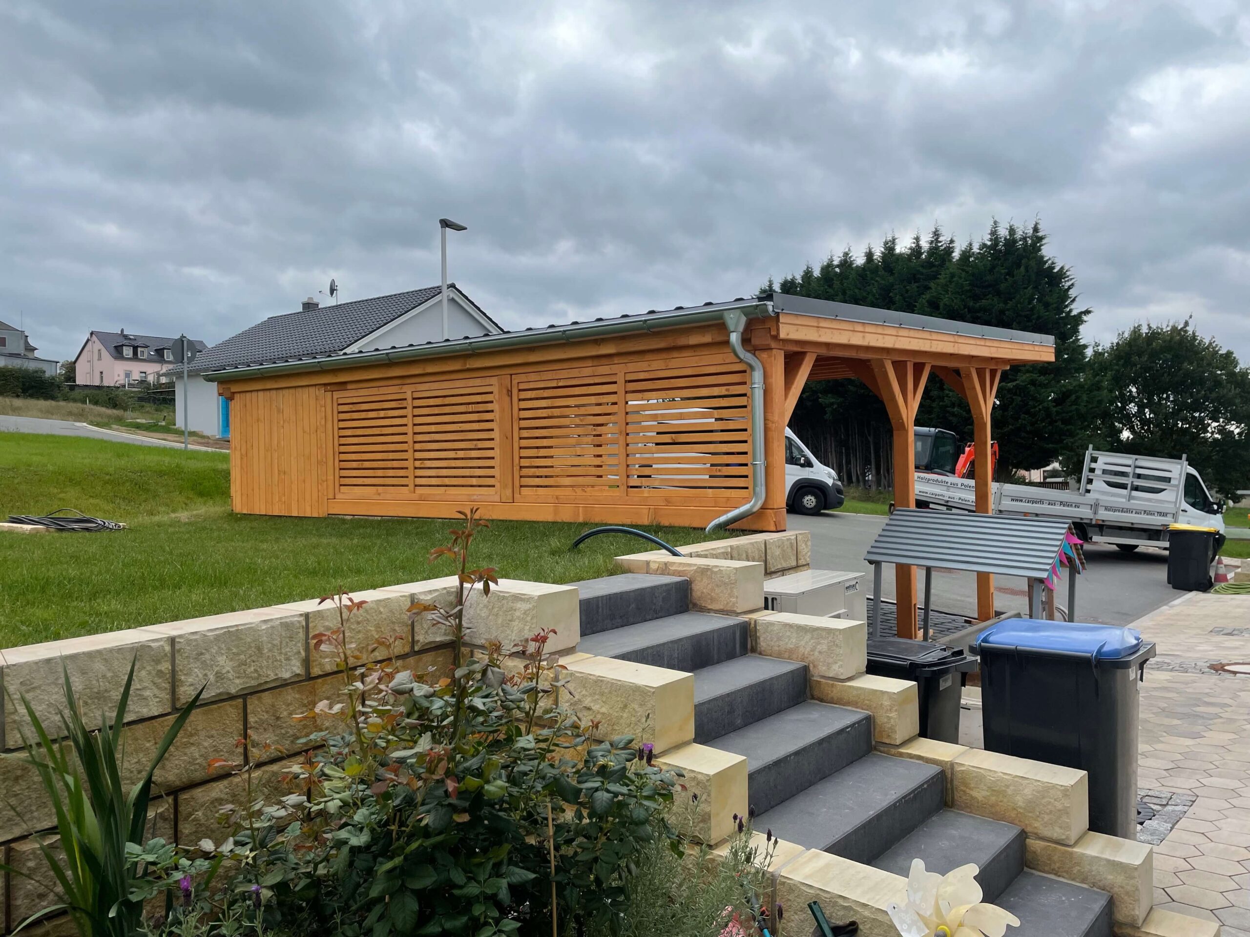 Rückseite des Carports mit Lamellenwand aus imprägniertem Holz, handgefertigt. Die vertikale Struktur verleiht Tiefe und moderne Leichtigkeit.