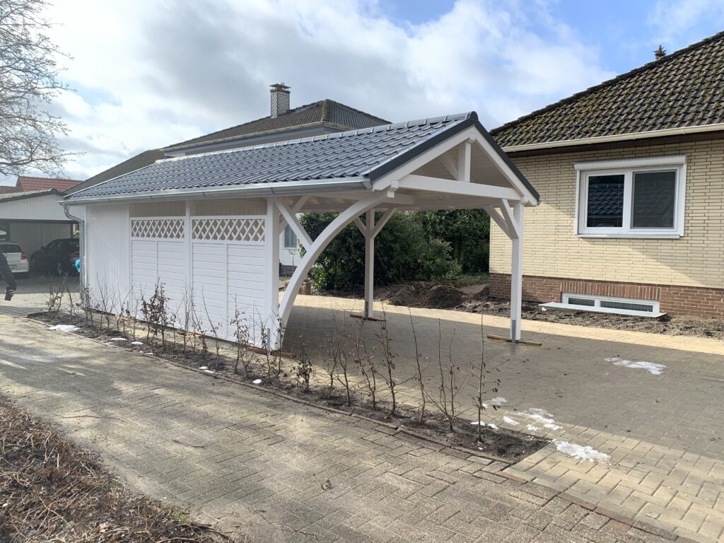 Einzelcarport Country mit vertikaler Wandverkleidung und dekorativem Gittereinsatz. Der sanfte Rundbogen und die natürliche Holzstruktur betonen ländliche Eleganz.
