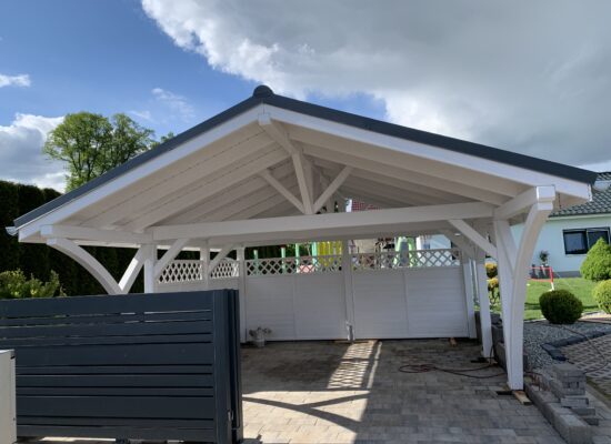 Frontansicht des weißen Doppelcarports mit anthrazitfarbenem Vivaldi-Dach und massiven Pfosten. Klassische Proportionen und handwerkliche Präzision in jedem Detail.