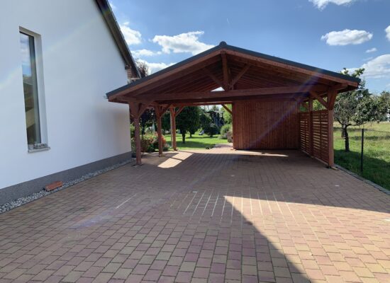 NaturaLine Carport im warmen Holzton, mit Satteldach, Lamellen-Sichtschutz und sichtbarer Holzmaserung. Harmonische Proportionen und solide Ausführung.