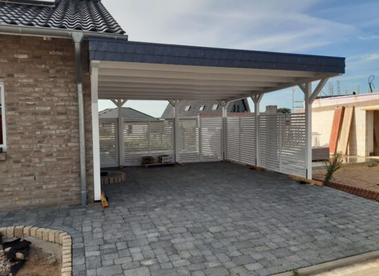 Weißer Doppelcarport mit Lamellenzaun, Walmdachblende und geschlossener Dachunterseite – handgefertigter Holzbau.