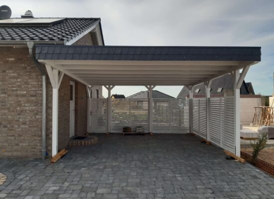 Doppelcarport Weiß mit Walmdachblende, direkt am Haus, gefertigt in solider Handwerksqualität.