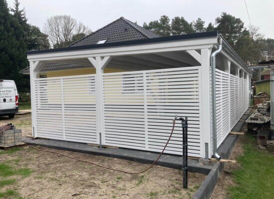 Seitenansicht des Carport Plus, zeigt die erweiterte Struktur und elegante Lamellenpaneele. Die weiße Holzoberfläche und klaren Linien vermitteln Ordnung und Ruhe.