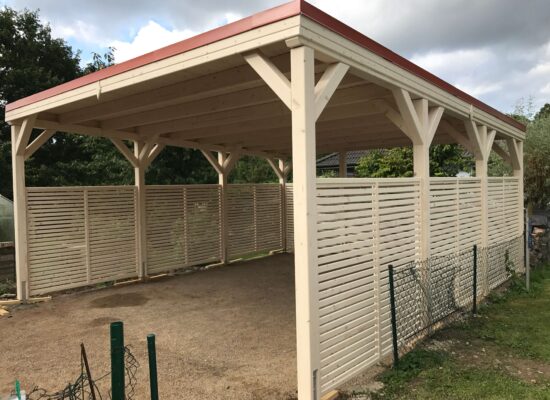 Flachdach-Carport CamperLine, extra hoch und massiv gebaut, hell imprägniertes Holz. Drei Seiten mit Lamellen als Windschutz – funktional und modern zugleich.