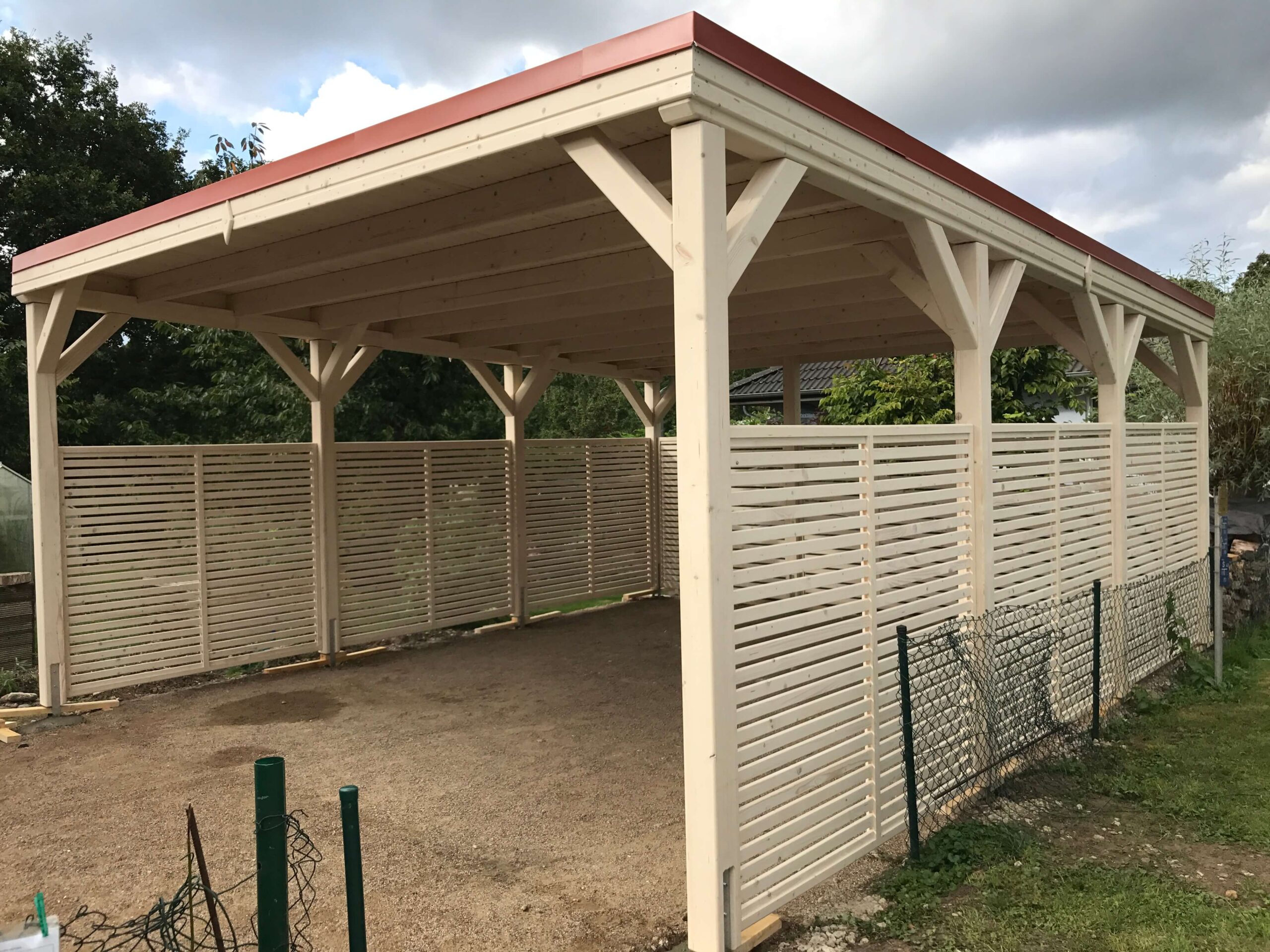 Flachdach-Carport CamperLine, extra hoch und massiv gebaut, hell imprägniertes Holz. Drei Seiten mit Lamellen als Windschutz – funktional und modern zugleich.