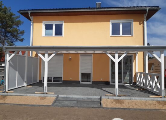 Weiße Terrassenüberdachung mit transparentem Dach und beidseitiger Gestaltung – Windschutz links, Kreuzgeländer rechts. Lichtdurchflutet und elegant.