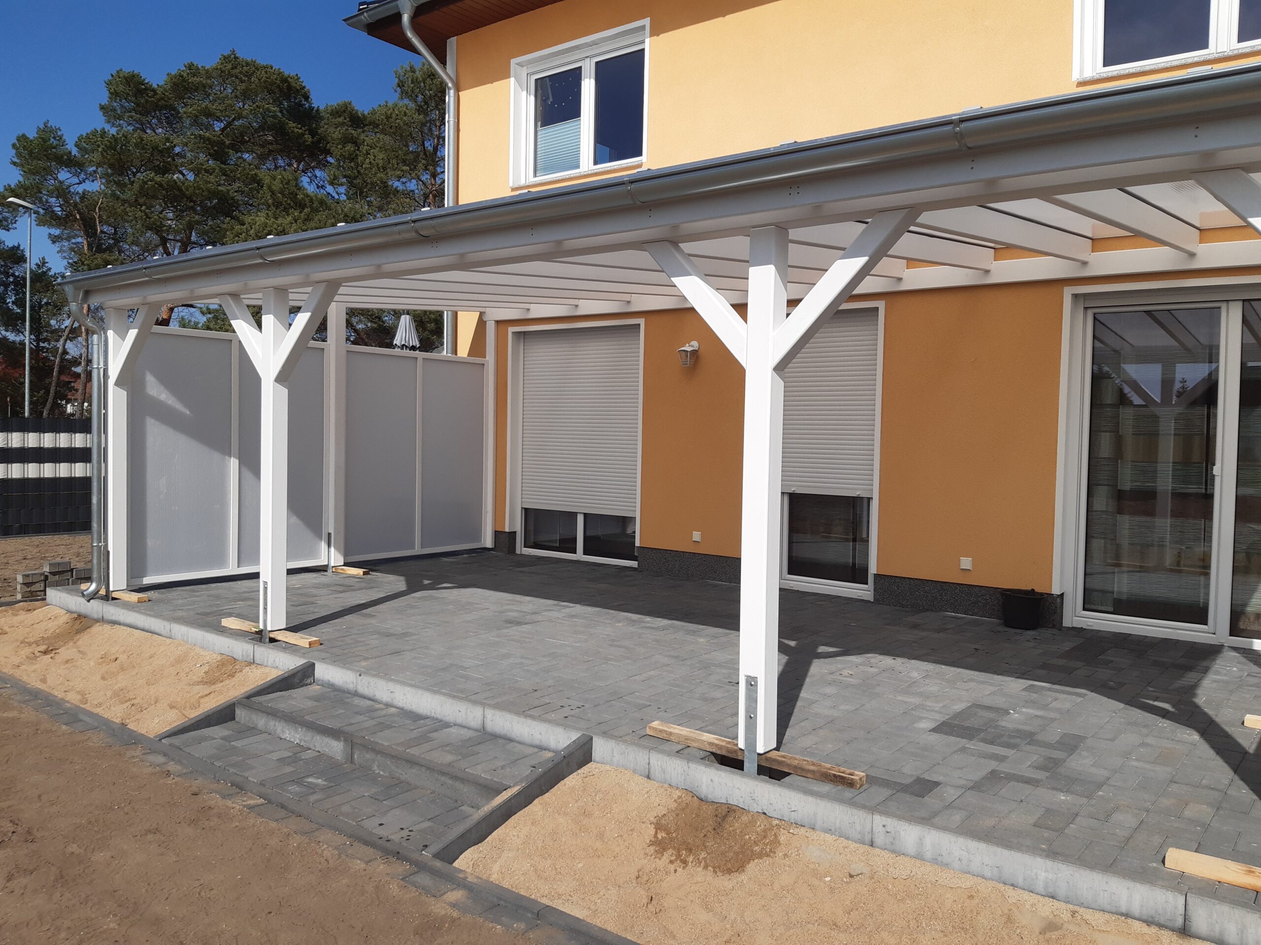 Seitenansicht der weißen Terrassenüberdachung mit milchigem Windschutz. Klare Linien, hochwertiges Handwerk und dezente Lichtwirkung.