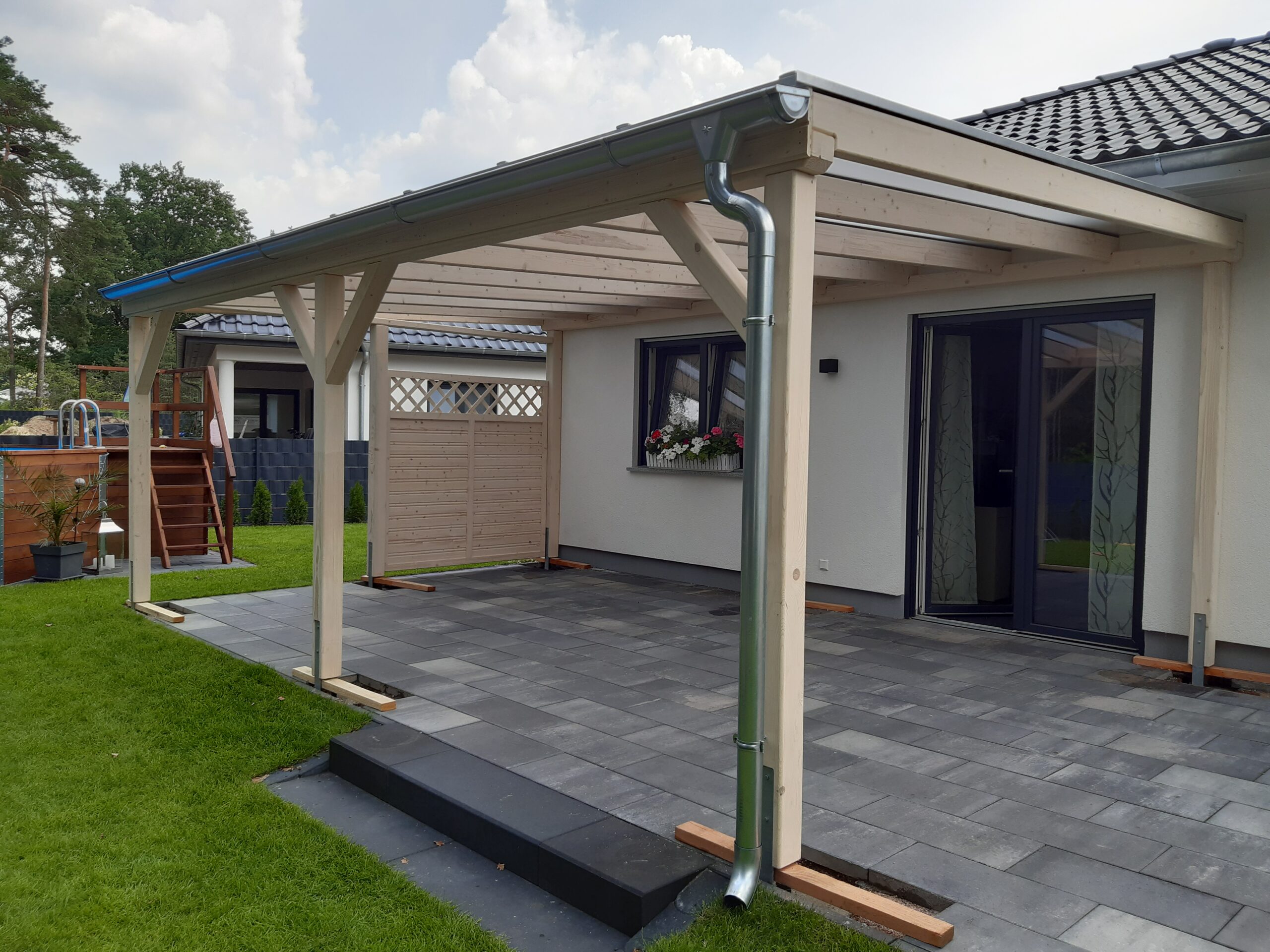 Terrassenüberdachung mit milchiger Doppelstegplatte und heller Holzstruktur. Klassische Linienführung und offene Seiten für luftige Atmosphäre.