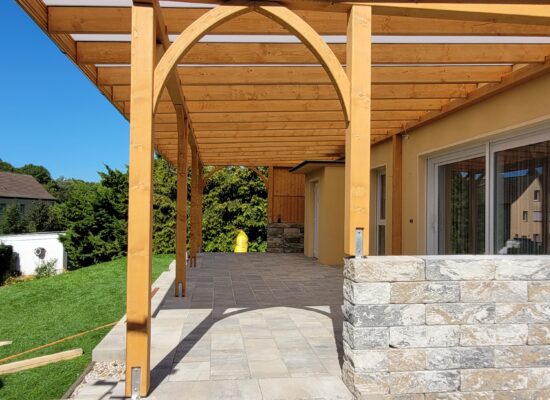 Große klassische Terrassenüberdachung aus Holz mit milchiger Doppelstegplatte und eleganten Bögen. Die natürliche Holzstruktur verleiht Wärme und Authentizität.