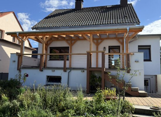 Maßgefertigte Terrassenüberdachung mit 14-cm-Holzpfosten auf großer Höhe. Handwerklich präzise errichtet über anspruchsvollem Gelände.