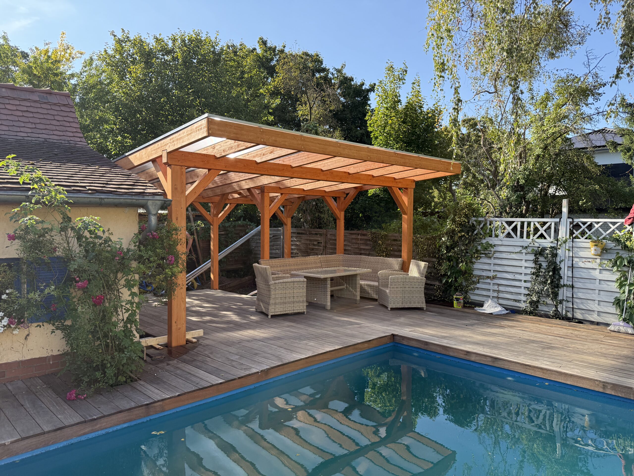 Große Pool-Terrassenüberdachung im Einklang mit dem Grundstück und Poolbereich. Die klare Holzstruktur und transparente Dachfläche fügen sich harmonisch in die Umgebung ein.