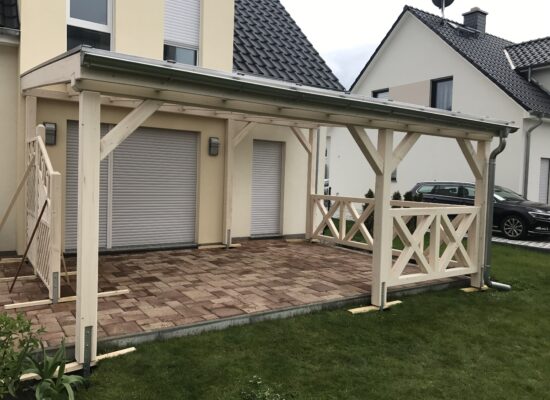 Terrassenüberdachung aus hell imprägniertem Holz mit schrägem Füllfeld und Kreuzgeländer. Maßarbeit mit Liebe zum Detail und sichtbarer Holzstruktur.