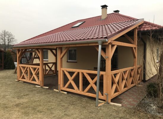 Handgefertigte Terrassenüberdachung aus Holz mit Vivaldi-Blechdach und Kreuzgeländer. Klassische Optik, massive Bauweise und präzise Ausführung.