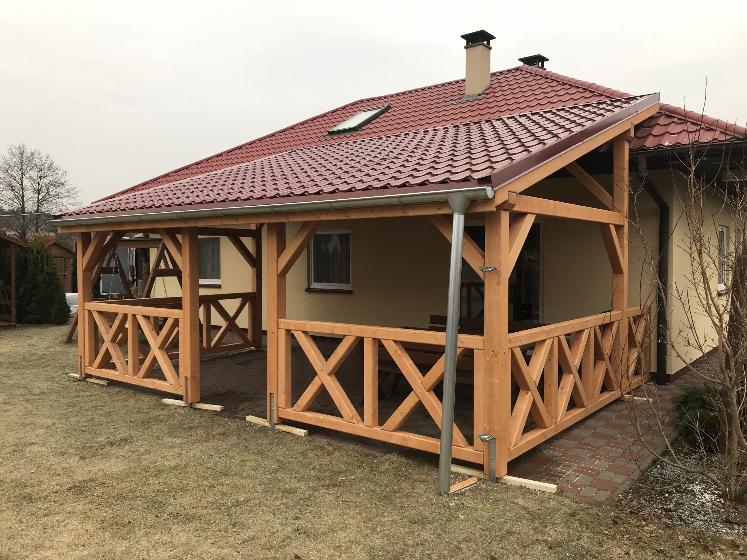 Handgefertigte Terrassenüberdachung aus Holz mit Vivaldi-Blechdach und Kreuzgeländer. Klassische Optik, massive Bauweise und präzise Ausführung.