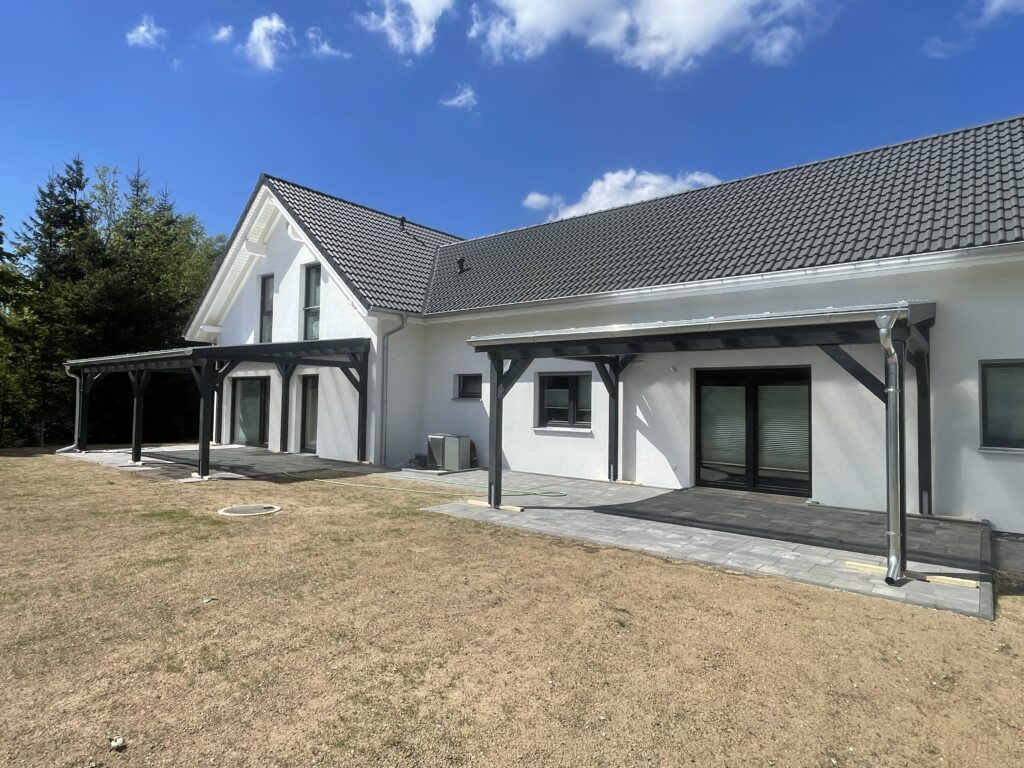 Anthrazitfarbene Terrassenüberdachungen mit transparenter Doppelstegplatte, passgenau am Gebäude montiert. Zeitloses Design mit handwerklicher Präzision.