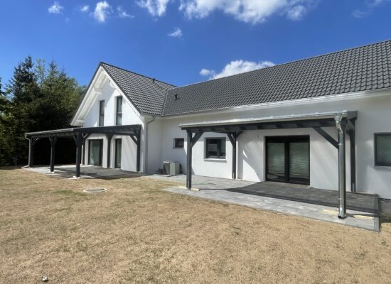 Anthrazitfarbene Terrassenüberdachungen mit transparenter Doppelstegplatte, passgenau am Gebäude montiert. Zeitloses Design mit handwerklicher Präzision.