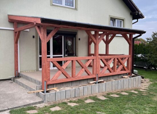 Handgefertigte Terrassenüberdachung aus imprägniertem Holz mit 14-cm-Stützen, Kreuzgeländer und milchiger Doppelstegplatte. Klassische Handwerksarbeit mit natürlicher Ausstrahlung.