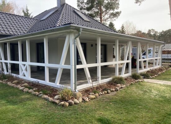 Komplettansicht der Fachwerk-Terrassenüberdachung rund ums Haus. Weiße Balken, anthrazitfarbenes Dach und harmonische Integration ins Gesamtbild.
