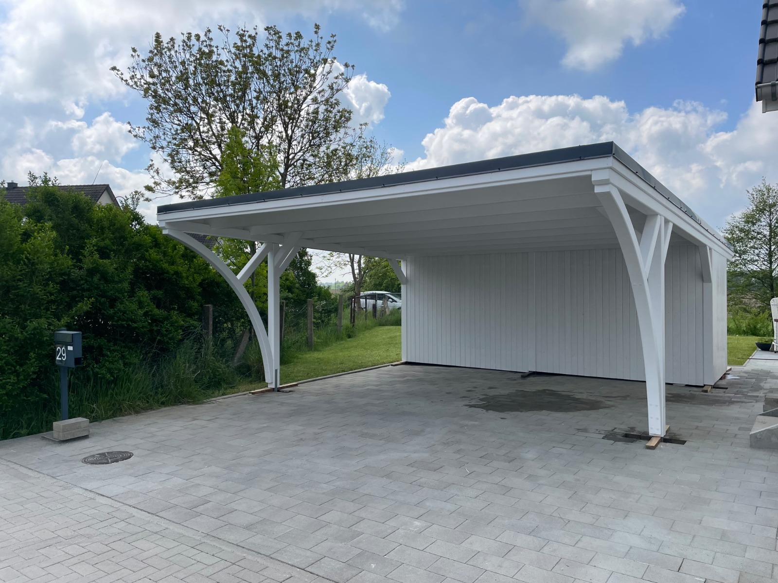 Doppelcarport mit Walmdachblende und seitlichem Zaunelement. Weiß-Anthrazit-Kombination und klare Linien betonen modernes Design und Handwerksqualität.